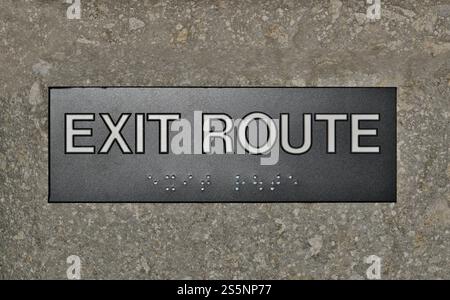 Exit route sign with braille symbols concrete wall interior evacuation. Stock Photo