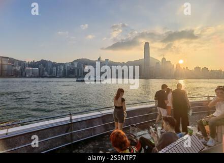 Hong Kong - November 17, 2024 : Golden hour sunset over a vibrant cityscape.  People gather on a waterfront promenade, enjoying the view.  A calm harb Stock Photo