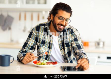 Positive arab guy having breakfast, using digital tablet, copy space Stock Photo