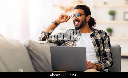Dreamy arab guy freelancer working from home, using laptop Stock Photo