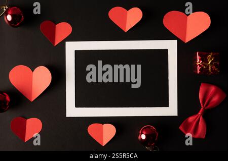 White photo frame and red heart paper pasted on a black background. Stock Photo