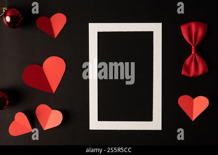 White photo frame and red heart paper pasted on a black background. Stock Photo