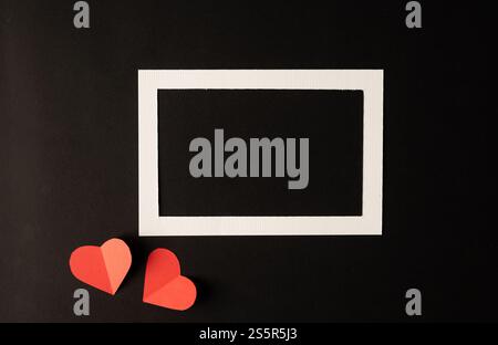 White photo frame and red heart paper pasted on a black background. Stock Photo