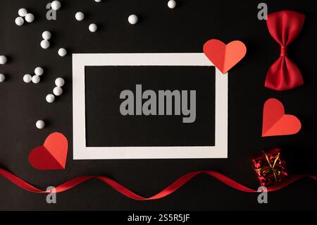 White photo frame and red heart paper pasted on a black background. Stock Photo