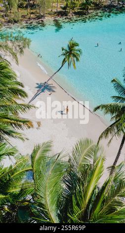 Warm sunlight glistens on the turquoise waters as a couple walks hand in hand on the pristine beach. Lush palm trees sway gently in the tropical breeze, creating a peaceful paradise. Stock Photo