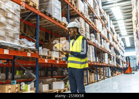 African man with reflective clothes and helmet using the digital tablet in a warehouse Stock Photo