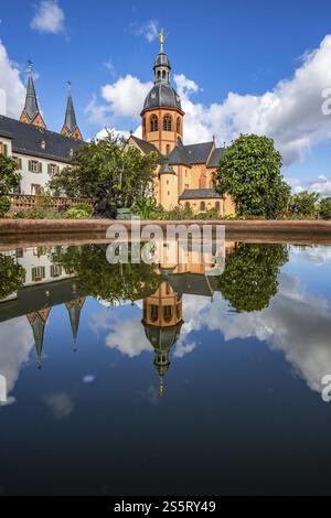 A historic monastery in the morning. Monastery walls, church and buildings are reflected in the water of a fountain. Beautiful garden in Seligenstadt Stock Photo