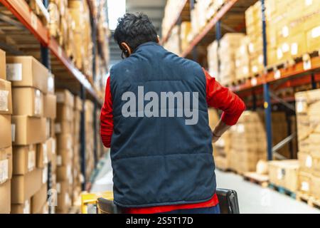 Rear view of a latin male worker pushing an hydraulic hand pallet truck on a warehouse Stock Photo