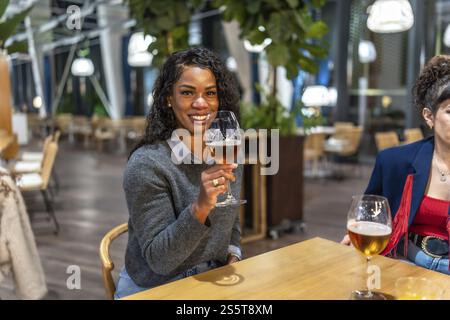 Latin woman enjoying beer talking to friends sitting on the terrace of a night bar Stock Photo