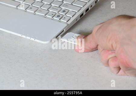 A male hand inserts a white compact SD card into the corresponding input in the side of the white netbook. Man uses modern technologies to store Stock Photo