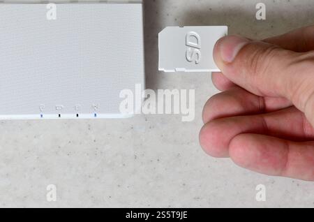 A male hand inserts a white compact SD card into the corresponding input in the side of the white netbook. Man uses modern technologies to store Stock Photo