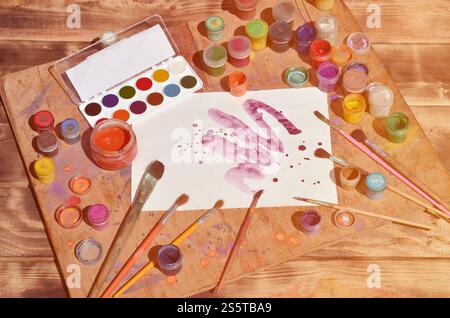 Background image showing interest in watercolor painting and art. A painted sheet of paper, surrounded by brushes, jars of watercolor paint and Stock Photo