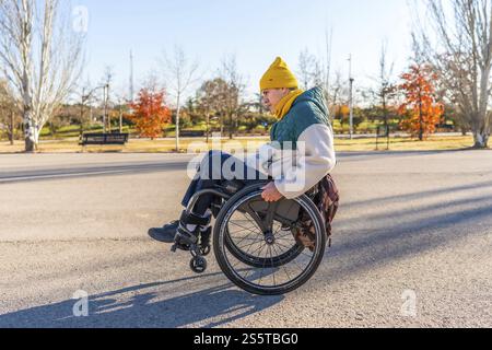 Person navigating a park pathway in a modern wheelchair, embracing the outdoors during a sunny autumn day Stock Photo