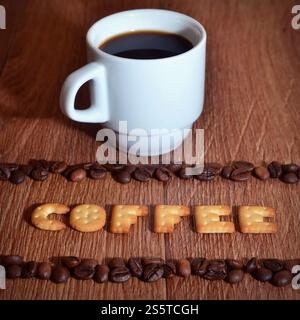 Still life with a small white cup of hot coffee and a salt cracker in the form of letters forming the word Coffee", framed by rows of coffee beans on Stock Photo