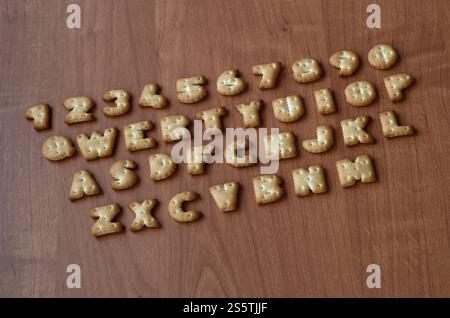 Letters of salty crackers lay on a wooden brown surface in the order similar to the layout of the buttons on the computer keyboard. Funny imitation Stock Photo