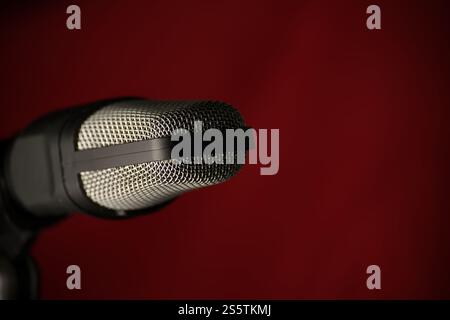 Professional studio microphone with metal mesh grille against dark red background, ideal for music recording, podcasting, and broadcasting Stock Photo