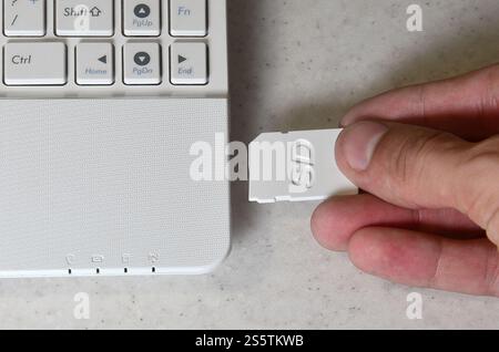 A male hand inserts a white compact SD card into the corresponding input in the side of the white netbook. Man uses modern technologies to store Stock Photo