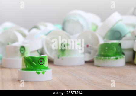 Several plastic nozzles from a paint sprayer that lie on a wooden surface against a gray wall background. The caps are smeared in green paint. The Stock Photo