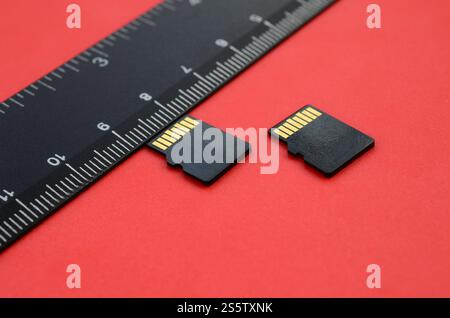 Two small micro SD memory cards lie on a red background next to a black ruler. A small and compact data and information store Stock Photo