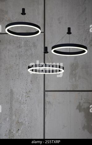 Unusual light sources hang on the background of a marble wall. Lamps in the form of a luminous ring Stock Photo