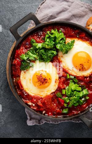 Shakshuka eggs in a pans with bread on a dark background. Poached eggs in a spicy tomato pepper sauce. Traditional Jewish scrambled eggs. Top view. Stock Photo