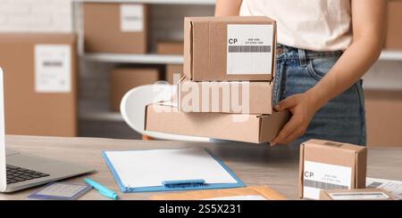 Female postal worker putting parcel boxes on table in warehouse Stock Photo
