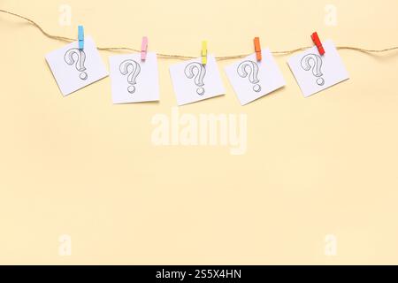 Sticky notes with question marks hanging on rope against color background Stock Photo