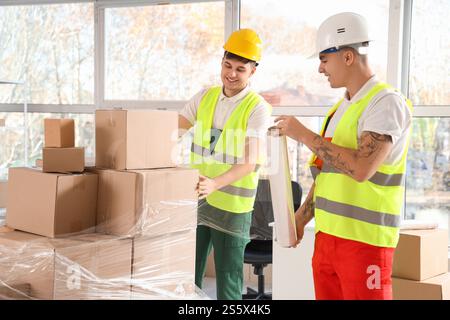 Male loaders wrapping boxes with stretch film in warehouse Stock Photo