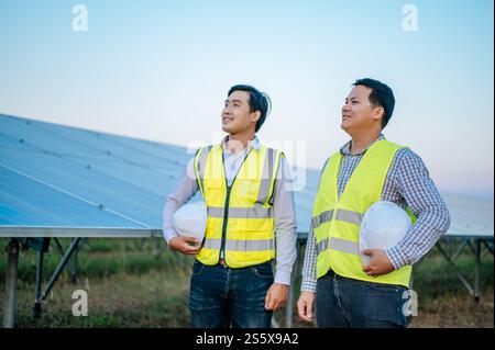 Portrait two young asian engineers standing holding white helmet and looking forward with smile, solar panels on background, copy space Stock Photo