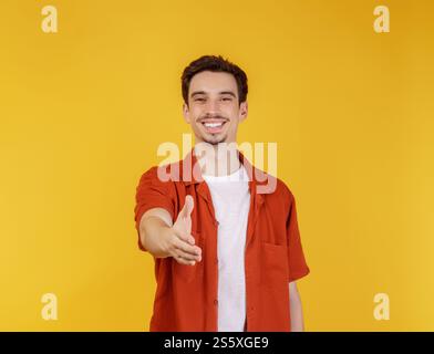Portrait of smiling handsome man extend hand for handshake, look friendly, greet you, hi gesture, standing over yellow background Stock Photo