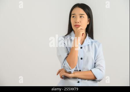 Portrait of Young asian woman in blue shirt thinking and looking up isolated on white background. Expression and lifestyle concept. Stock Photo