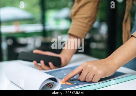Close up, Young woman use smartphone while working on laptop and paperwork or report presenting Project growth graph at cafe Stock Photo