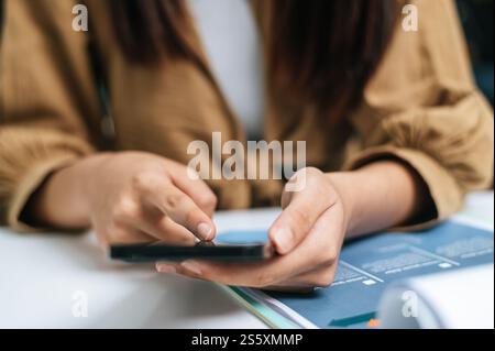 Selective focus, Close up finger of Young woman use smartphone while working on laptop and paperwork or report presenting Project growth graph at cafe Stock Photo