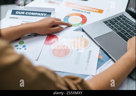 Selective focus, close up hands of Young woman use smartphone while working on laptop and paperwork or report presenting Project growth graph at cafe Stock Photo