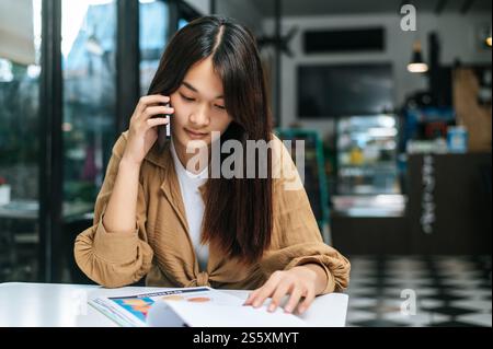 Close up, Young woman use smartphone while working on laptop and paperwork or report presenting Project growth graph at cafe Stock Photo