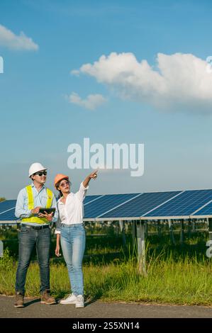 Asian Young Inspector Engineer man and female colleague wearing helmet and sunglasses use tablet to checking operation in solar station, copy space Stock Photo