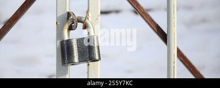 A large gray padlock hangs on a metal gate Stock Photo