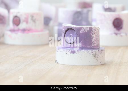 Several plastic nozzles from a paint sprayer that lie on a wooden surface against a gray wall background. The caps are smeared in violet paint. The Stock Photo