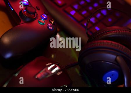 Modern gamepad and gaming mouse lies with keyboard and headphones on table in dark playroom scene close up. Background composition for video gaming Stock Photo