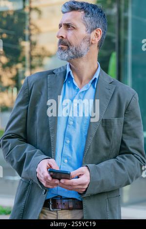 Thoughtful Man Holding Smartphone in Urban Setting Vertical Stock Photo
