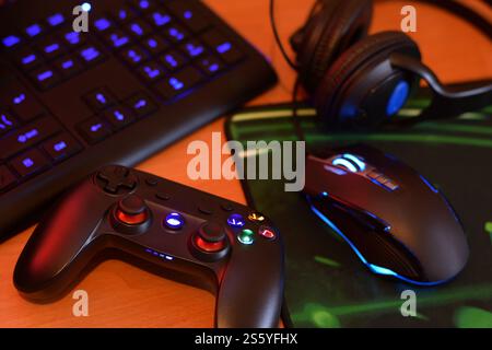 Modern gamepad and gaming mouse lies with keyboard and headphones on table in dark playroom scene close up. Lets play video games together with Stock Photo