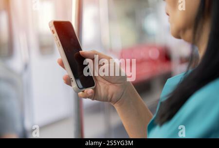 Cropped shot of Asian woman using cellphone inside train compartment. Selective focus on hand. Stock Photo