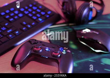 Modern gamepad and gaming mouse lies with keyboard and headphones on table in dark playroom scene close up. Devices for playing video games at home. Stock Photo