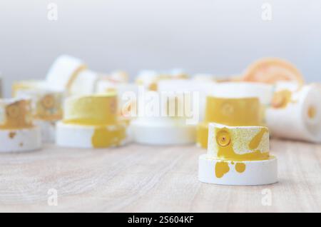 Several plastic nozzles from a paint sprayer that lie on a wooden surface against a gray wall background. The caps are smeared in yellow paint. The Stock Photo