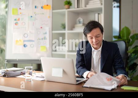 Elderly businessman reviewing financial reports while analyzing data in a modern office Stock Photo