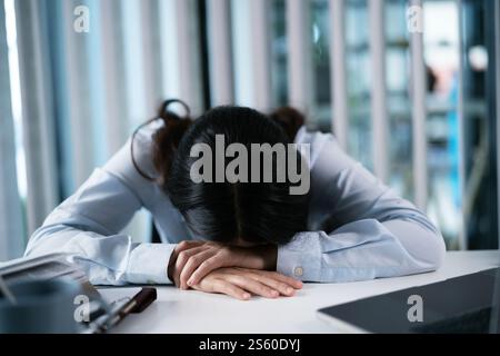 Alone Working Late. Asian business woman at workplace in office  laid her head down on the table fell asleep in front of laptop. Stock Photo