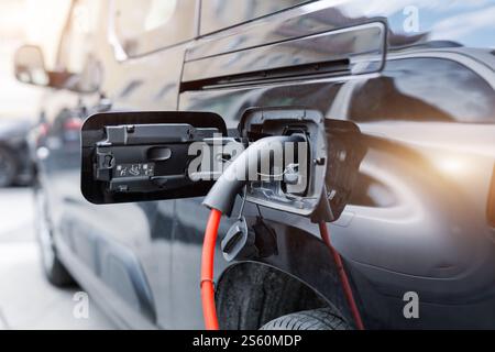 Close-up modern electric plug-in hybrid car van parked near fast charger charging station point center street old European city. Eco friendly green Stock Photo