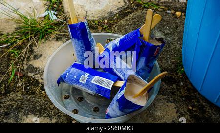 A bowl filled with empty ice cream wrappers and wooden sticks on a concrete surface. Stock Photo