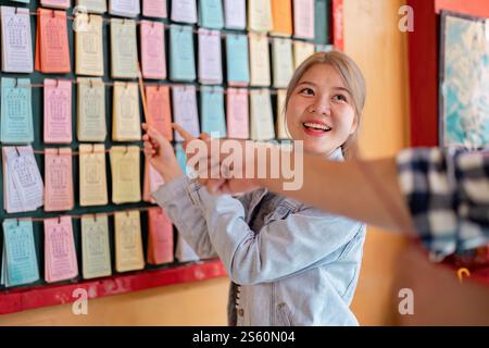 Young woman enthusiastically explaining traditional calendar concepts while guiding a friend in a vibrant cultural setting Stock Photo