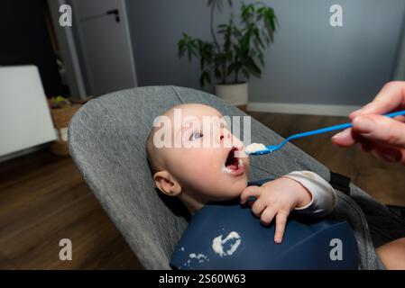 A mother feeding her baby semolina using a plastic spoon. Stock Photo